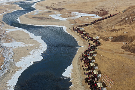 stream of pilgrims walking beside a river with snow on its banks